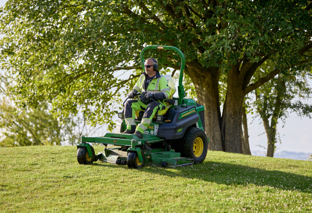 KENDA K505 tire mounted on John Deere zero-turn professional mower cutting grass under trees
