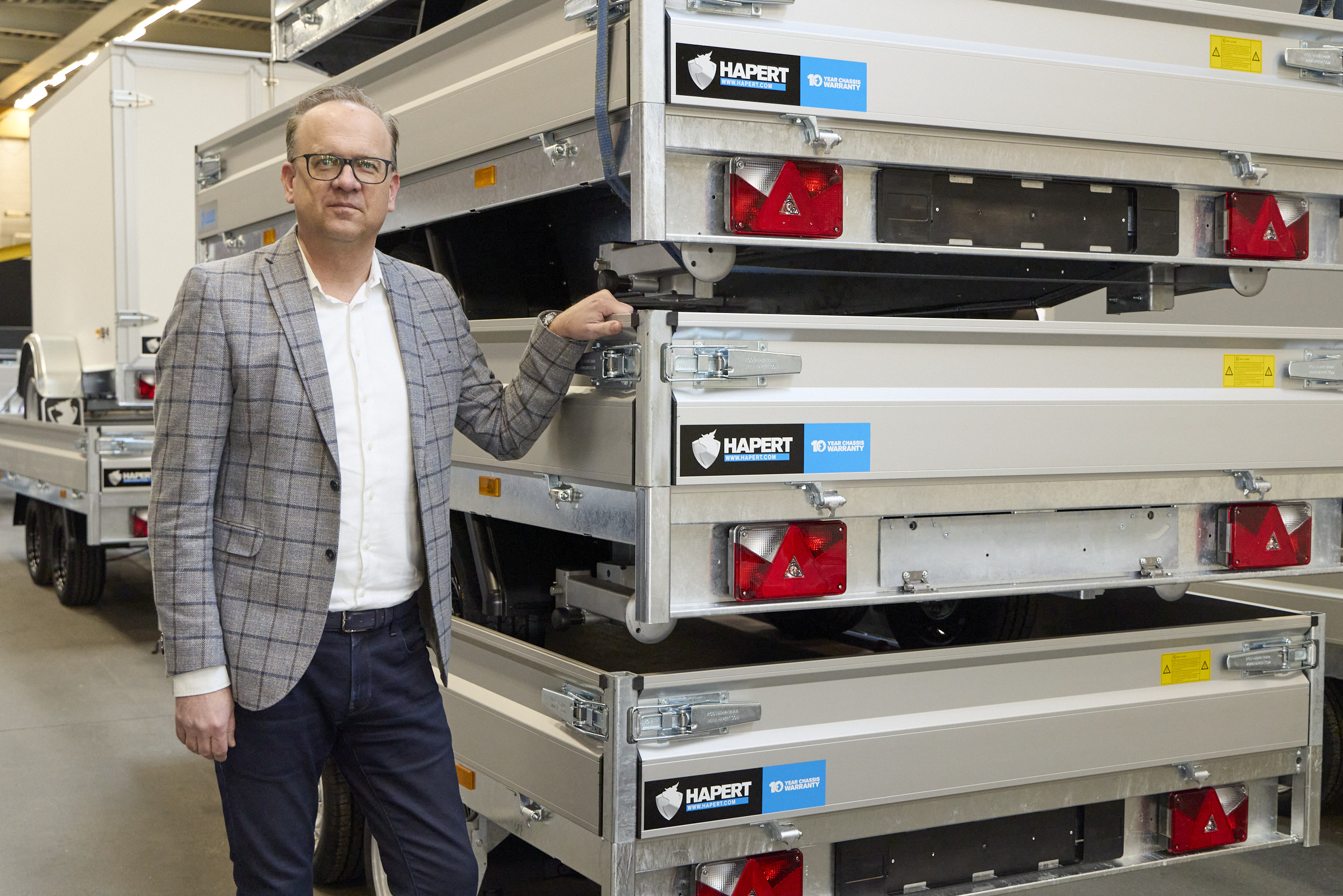 Der kaufmännische Leiter von Hapert Trailers steht neben seinen Anhängern und lächelt